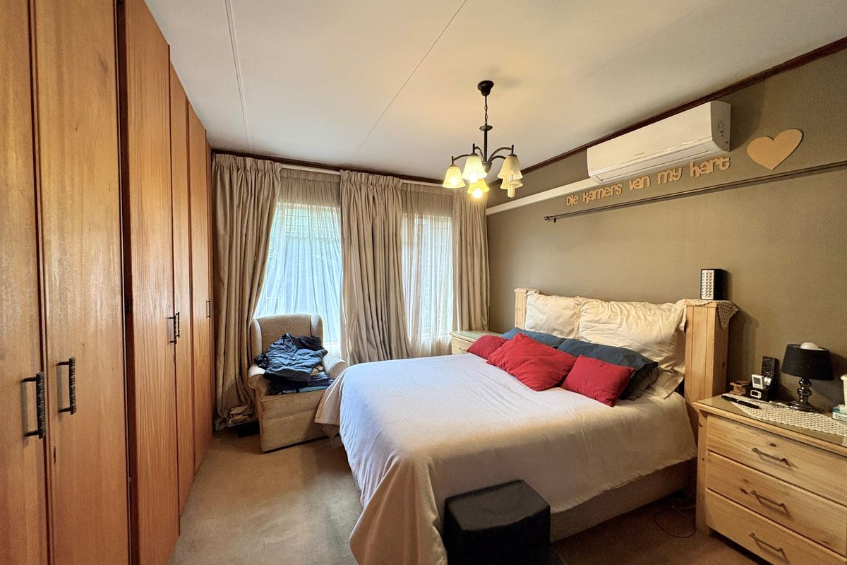 A well-proportioned bedroom featuring extensive built-in wooden cupboards, a split-system air conditioning unit, and neutral carpeting.