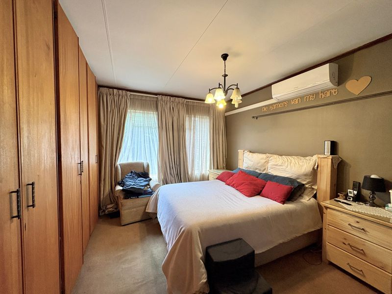 A well-proportioned bedroom featuring extensive built-in wooden cupboards, a split-system air conditioning unit, and neutral carpeting.