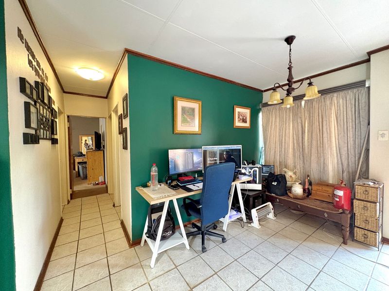 A multi-purpose living area featuring ceramic tiled flooring, a central chandelier, and a hallway leading to adjacent rooms.