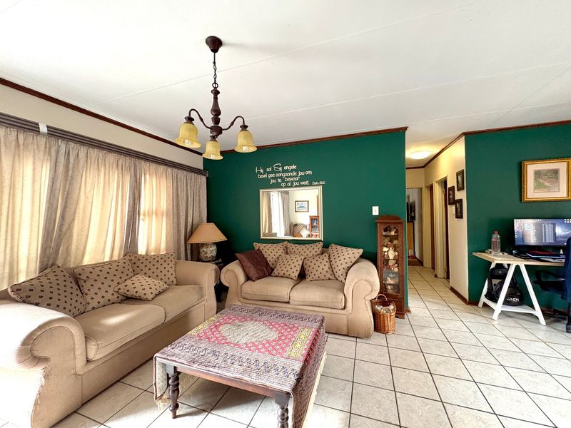 A living room featuring ceramic floor tiles, a central light fixture, and a bold green accent wall, providing a functional and well-lit living space.