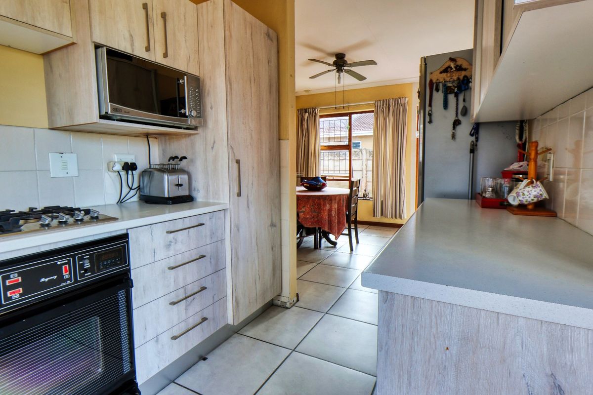 A functional kitchen featuring light wood-grain cabinetry, built-in oven and hob, tiled splashbacks, and tiled flooring, with an open flow to the adjacent dining area.