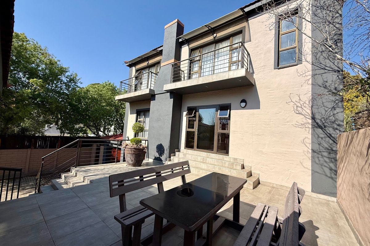 Rear exterior view of a two-story house featuring a paved patio area, upper-level balconies, and modern architectural finishes.