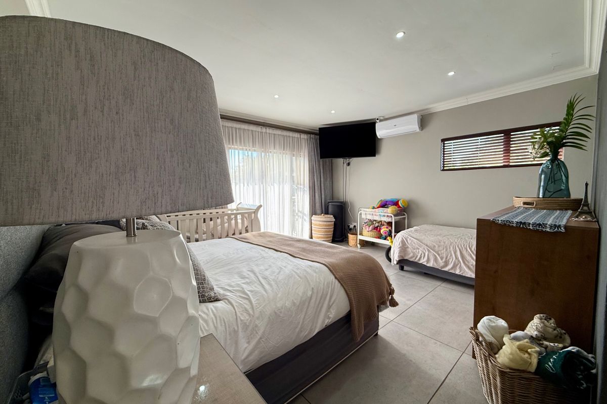 Spacious bedroom featuring large format floor tiles, recessed lighting, a wall-mounted air conditioning unit, and sliding glass doors providing natural light.