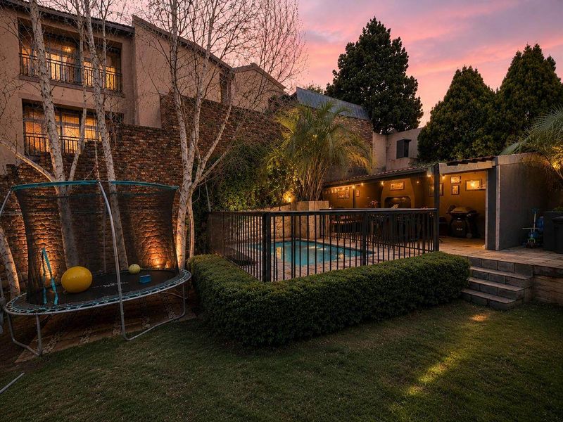 A beautifully landscaped rear garden featuring a fenced swimming pool, a covered patio area, and stone retaining walls, perfect for outdoor entertaining.