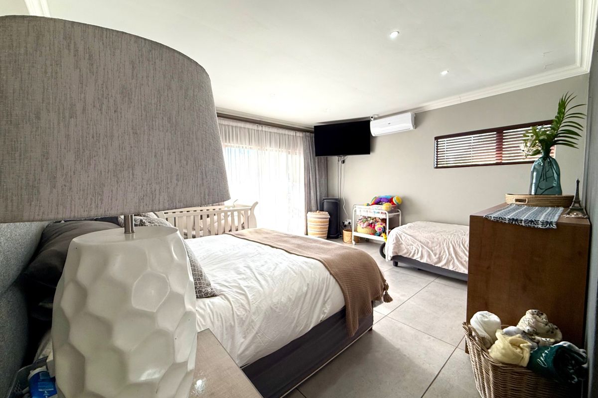 Spacious bedroom featuring large format floor tiles, recessed lighting, a wall-mounted air conditioning unit, and sliding door access to the exterior.