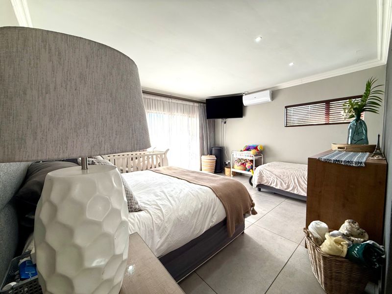 Spacious bedroom featuring large format floor tiles, recessed lighting, a wall-mounted air conditioning unit, and sliding door access to the exterior.
