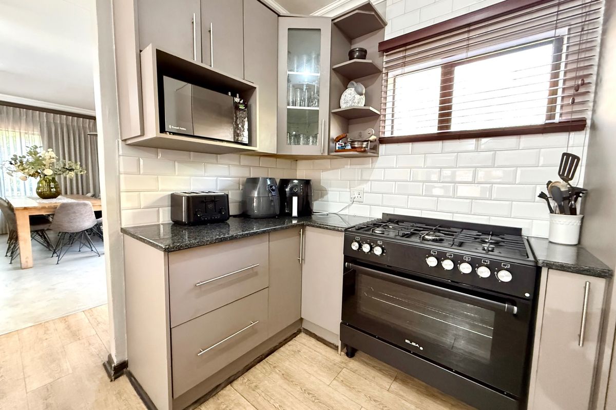 Modern kitchen featuring subway tile backsplash, granite countertops, and a black gas stove, with an open-plan layout leading to the dining area.