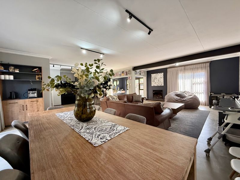 Spacious open-plan living and dining area featuring a fireplace, built-in shelving, and modern track lighting with access to the outdoor space.