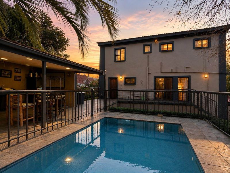 A well-maintained outdoor pool area featuring a tiled deck, metal safety fencing, and a covered patio space, perfect for evening relaxation.