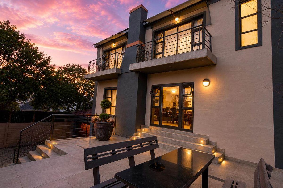 A beautifully lit rear exterior view featuring a tiled patio, upper-level balconies, and modern architectural lighting at dusk.