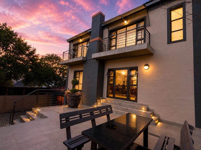 A beautifully lit rear exterior view featuring a tiled patio, upper-level balconies, and modern architectural lighting at dusk.