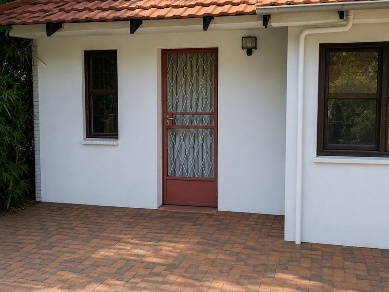 A well-maintained rear exterior view featuring a paved patio area, terracotta tiled roof, and secure entrance with a metal security gate.