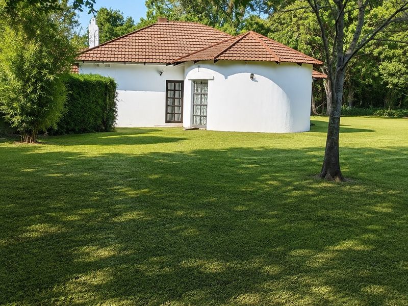 A view of the rear elevation of the house featuring a unique curved wall design, tiled roof, and expansive surrounding garden.