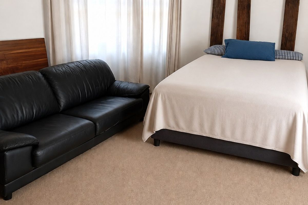 A bedroom featuring neutral carpet flooring, white walls, and a ceiling vent, providing a functional space with natural light from the window.
