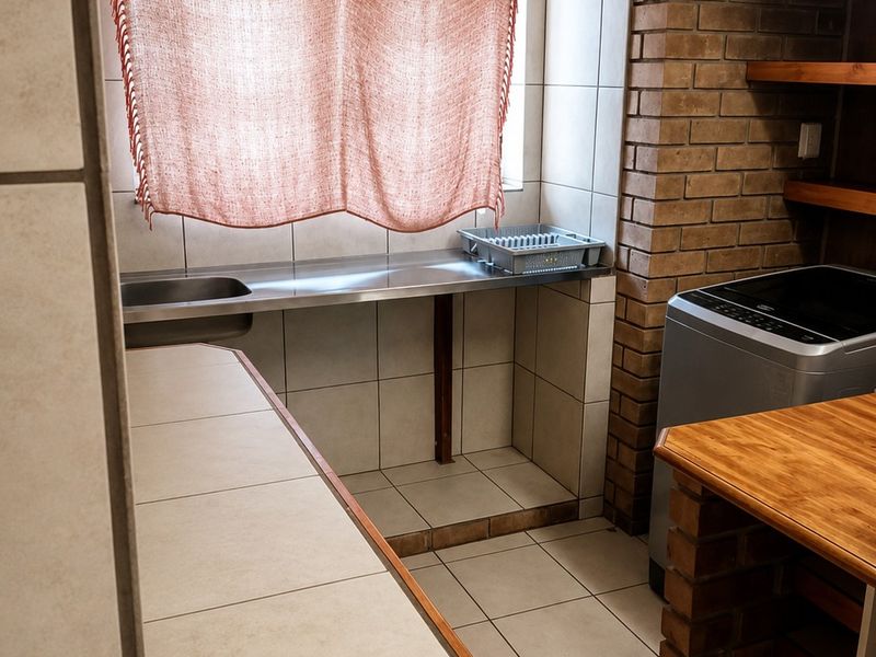 A functional laundry area featuring a stainless steel sink, tiled splashback, and brick wall accents with built-in shelving.