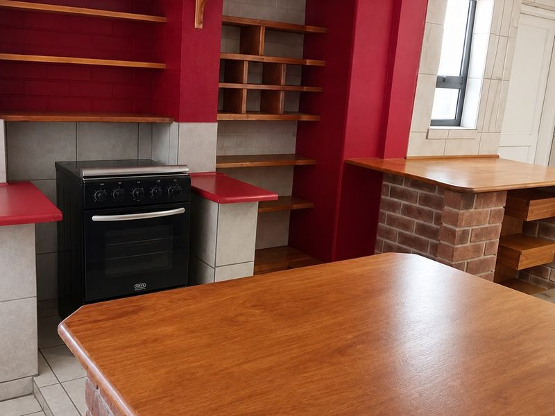 A kitchen featuring a brick island with a wooden countertop, built-in wooden shelving, and a freestanding stove against a red-painted wall.