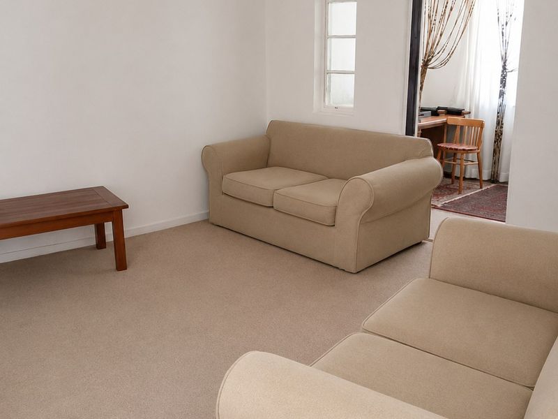 A neutrally painted living room featuring carpeted flooring and a multi-pane window, with an open doorway leading to an adjacent space.
