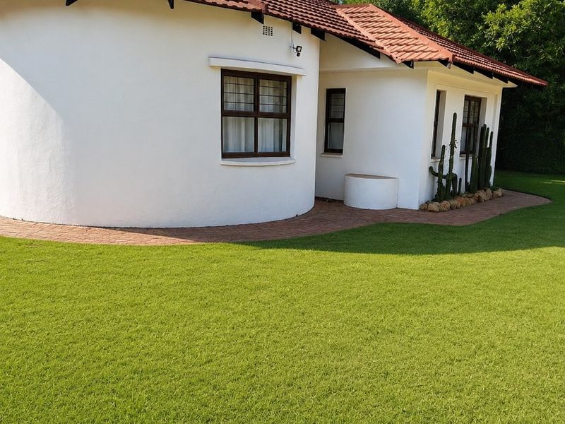 A well-maintained rear exterior view of the house featuring a unique curved wall design, terracotta roof tiles, and a neatly manicured lawn.