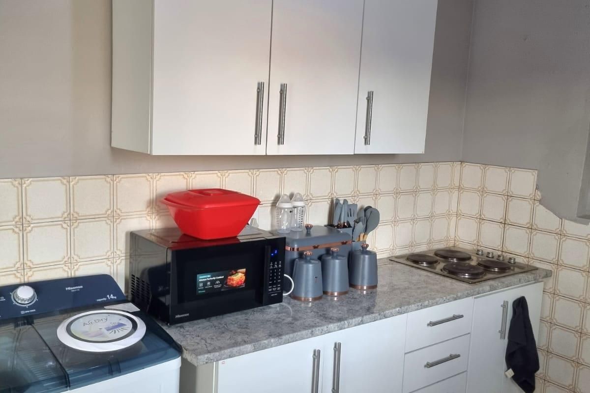 A functional kitchen area featuring white cabinetry, a laminate countertop, an integrated electric hob, and classic tiled splashbacks.