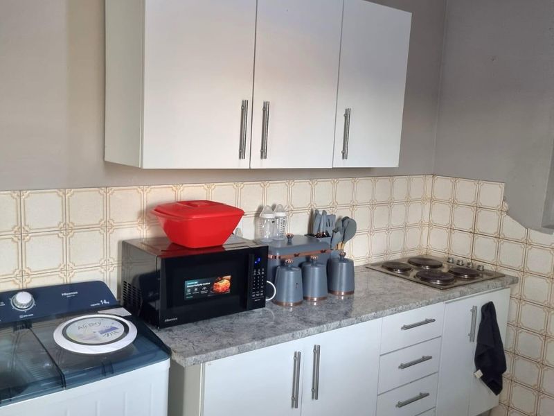 A functional kitchen area featuring white cabinetry, a laminate countertop, an integrated electric hob, and classic tiled splashbacks.