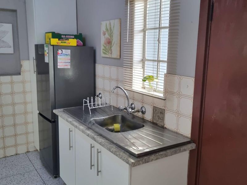 A compact kitchen area featuring a stainless steel sink, built-in cabinetry, and tiled backsplash, requiring cosmetic updates to modernize the space.