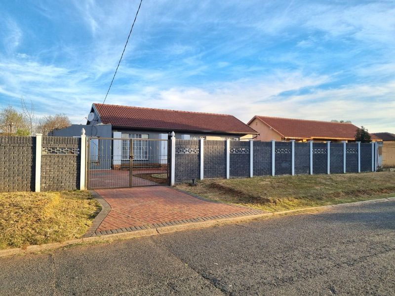 Front view of a residential property featuring a paved driveway, secure metal gate, and a decorative brick boundary wall.