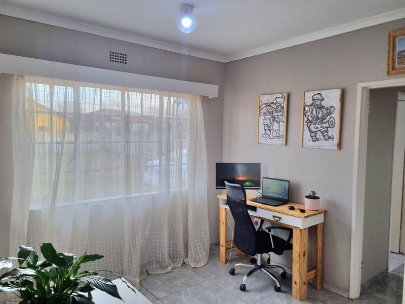 A functional home office space featuring neutral wall tones, tiled flooring, and a large window allowing for natural light.