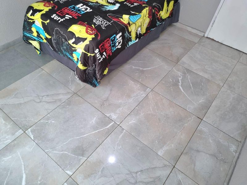 A bedroom featuring modern, large-format marble-look porcelain floor tiles throughout the space.