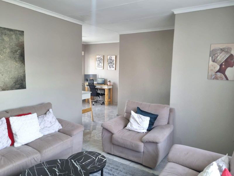 A neutrally painted living room featuring tiled flooring and coved ceilings, with an open transition to an adjacent study or office area.