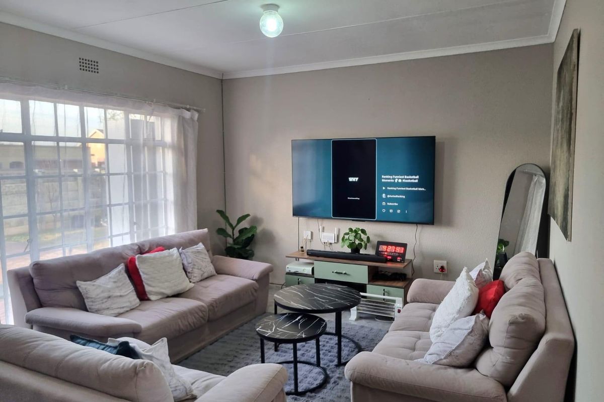 A comfortable living room featuring a large window, neutral wall tones, and a wall-mounted television setup.