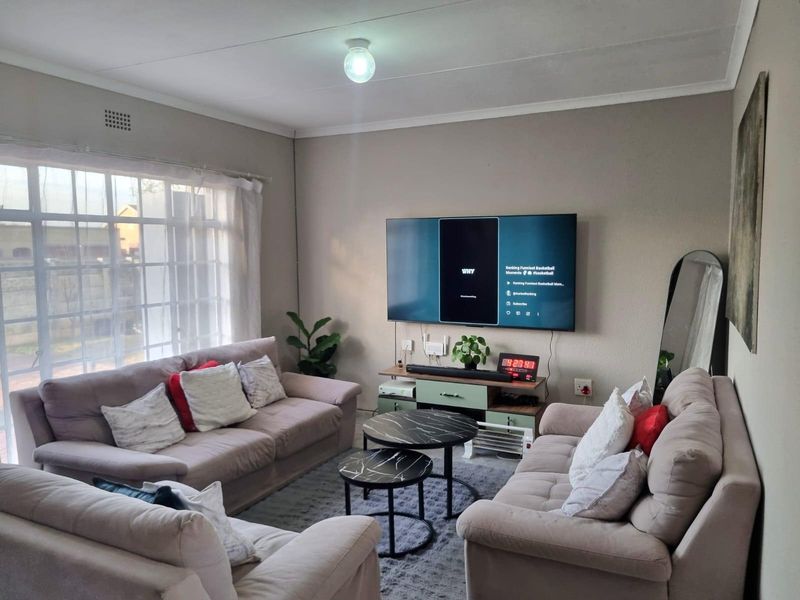 A comfortable living room featuring a large window, neutral wall tones, and a wall-mounted television setup.