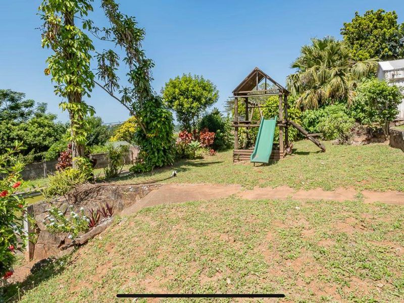 A sloped garden area featuring a stone retaining wall, mature trees, and a storage shed, offering potential for landscaping and outdoor development.