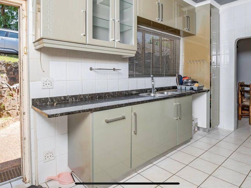 A functional kitchen featuring laminate cabinetry, tiled splashbacks, and tiled flooring, with direct access to the outdoor area.