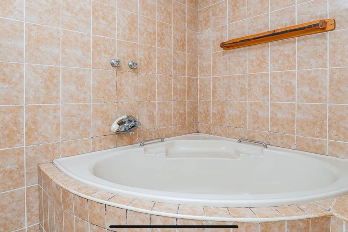 A dated bathroom featuring a corner bathtub with beige ceramic wall tiling and integrated plumbing fixtures.