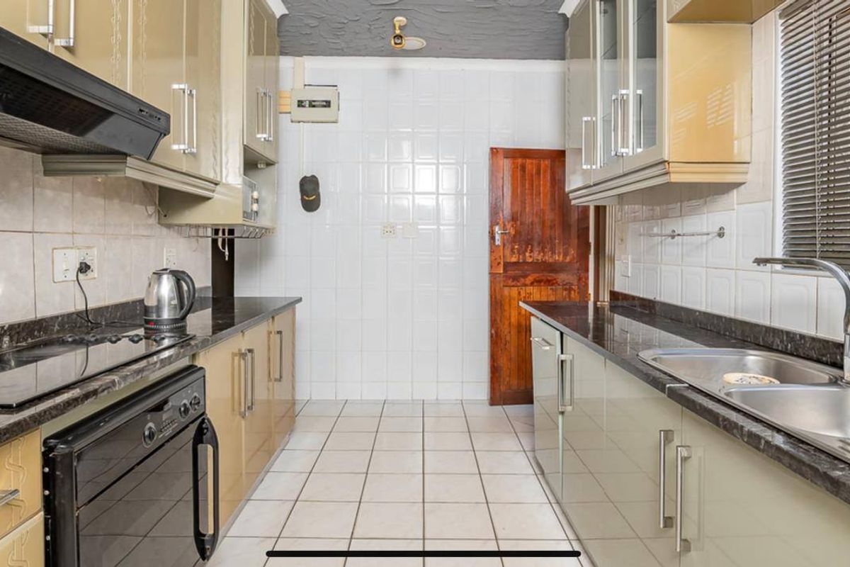 A functional galley-style kitchen featuring built-in cabinetry, granite countertops, a stainless steel sink, and an integrated oven with an extractor fan.