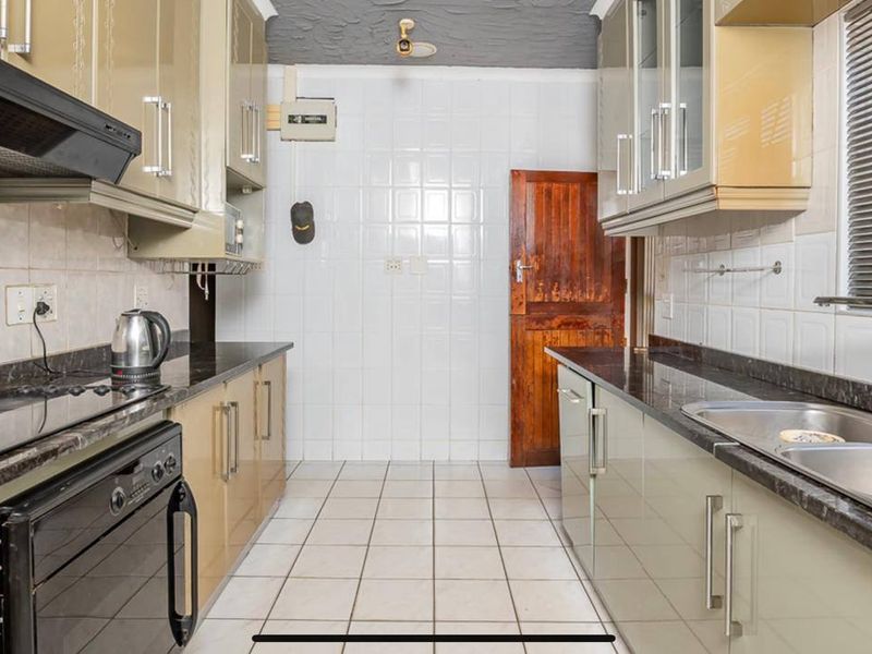 A functional galley-style kitchen featuring built-in cabinetry, granite countertops, a stainless steel sink, and an integrated oven with an extractor fan.