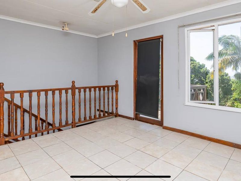 An open landing area featuring tiled flooring, a wooden balustrade, and access to an outdoor balcony through a sliding door.