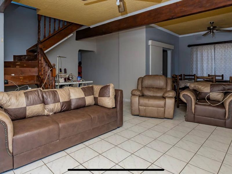 Open plan living area featuring ceramic floor tiles, exposed timber ceiling beams, and a timber staircase leading to the upper level.