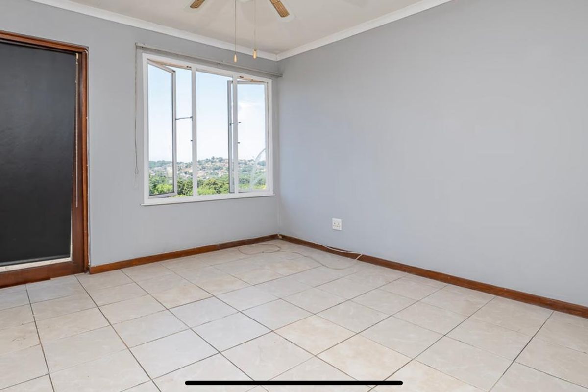 An empty bedroom featuring tiled flooring, a ceiling fan, and a window with views, providing a blank canvas for interior design.
