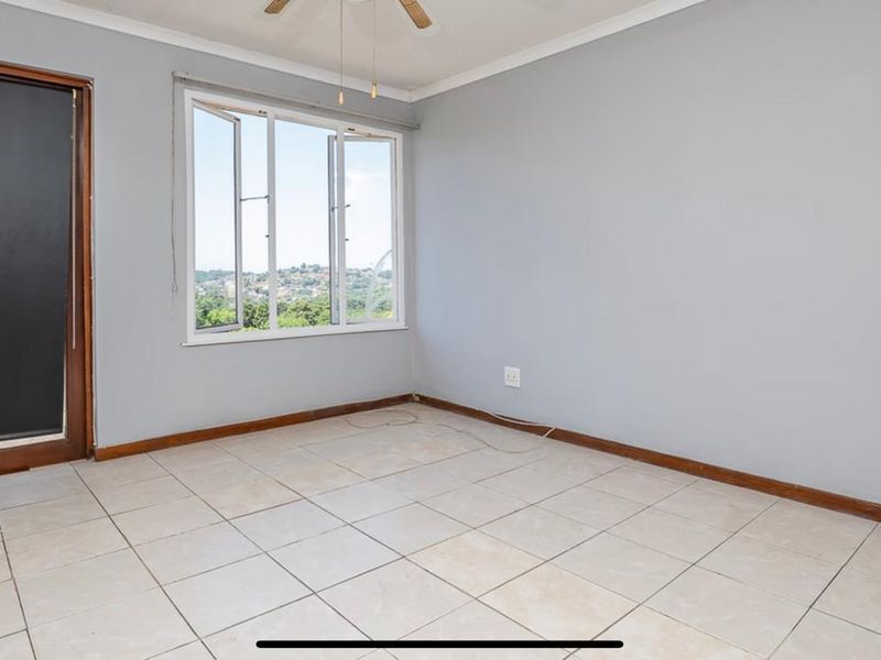 An empty bedroom featuring tiled flooring, a ceiling fan, and a window with views, providing a blank canvas for interior design.