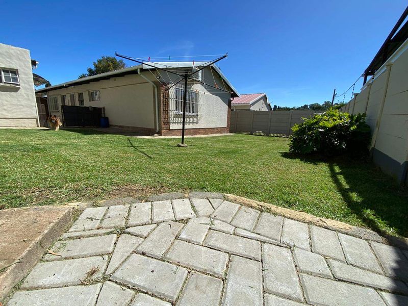 A rear garden area featuring a paved patio, established lawn, and perimeter boundary wall with security features.