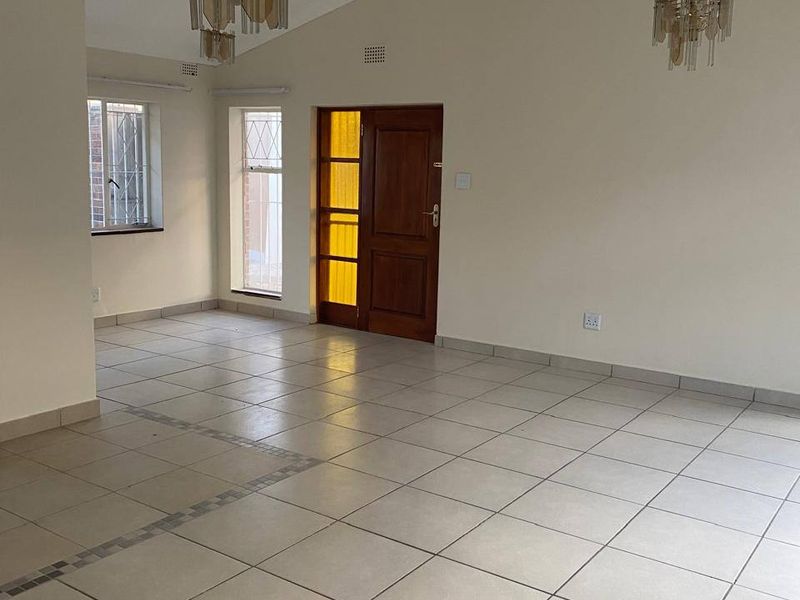 Spacious, light-filled living area featuring vaulted ceilings, tiled flooring, and a classic timber entrance door, offering a versatile blank canvas for interior design.