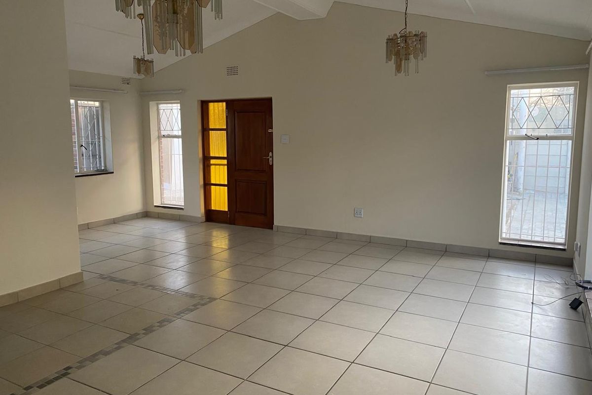 Spacious, light-filled living area featuring vaulted ceilings, tiled flooring, and large windows with security bars, offering a blank canvas for interior design.