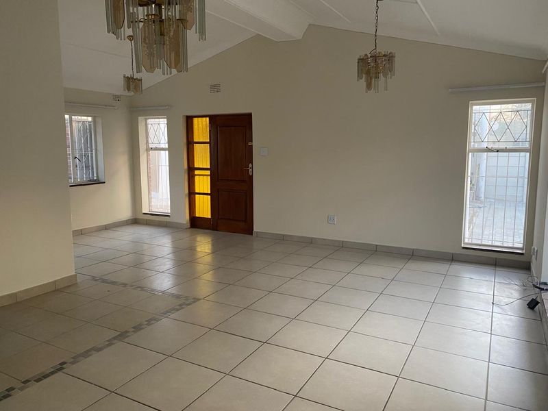 Spacious, light-filled living area featuring vaulted ceilings, tiled flooring, and large windows with security bars, offering a blank canvas for interior design.