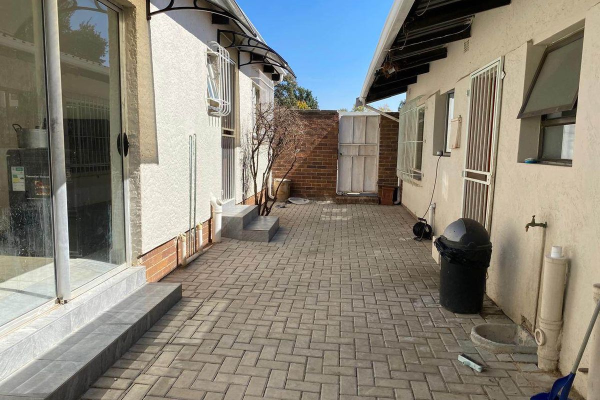A paved rear courtyard area featuring security gates, external plumbing, and access to the main dwelling via sliding glass doors.