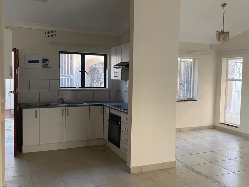 Open-plan kitchen and living area featuring tiled flooring, built-in cabinetry, integrated oven and hob, and security bars on windows.