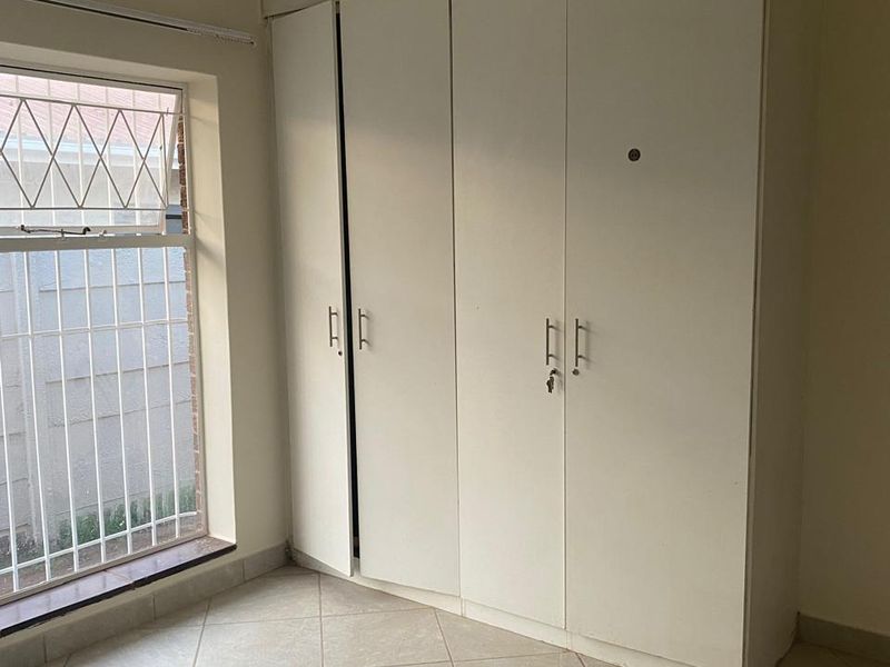 A bedroom featuring tiled flooring and a built-in wardrobe with security bars installed on the window.