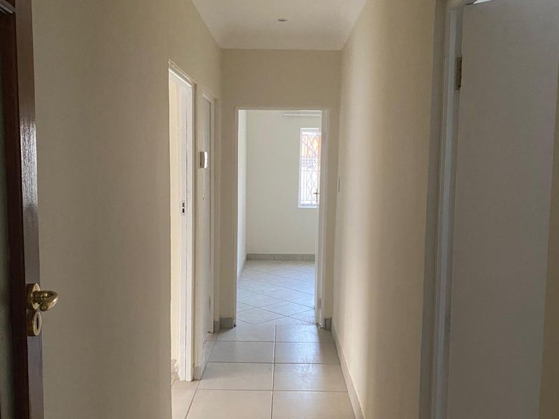 A clean, neutral hallway featuring tiled flooring and recessed lighting, providing access to multiple rooms within the home.
