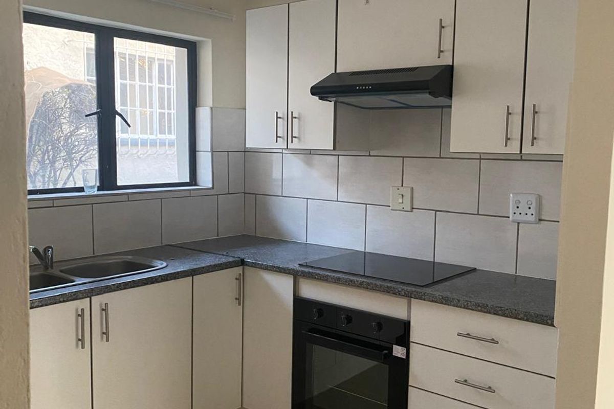 A functional kitchen featuring white cabinetry, dark laminate countertops, built-in oven, electric hob, and tiled splashback with neutral floor tiles.