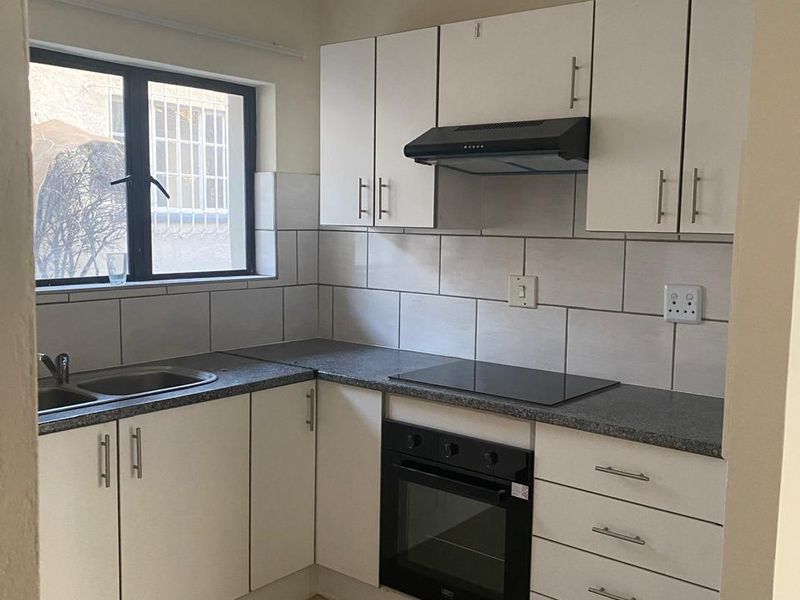 A functional kitchen featuring white cabinetry, dark laminate countertops, built-in oven, electric hob, and tiled splashback with neutral floor tiles.